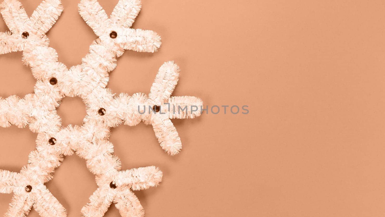 Fluffy white snowflake Christmas decor. Image toned in Peach Fuzz color of the year 2024. The concept of New Year and Christmas holidays, congratulations. Copy space. View from above.