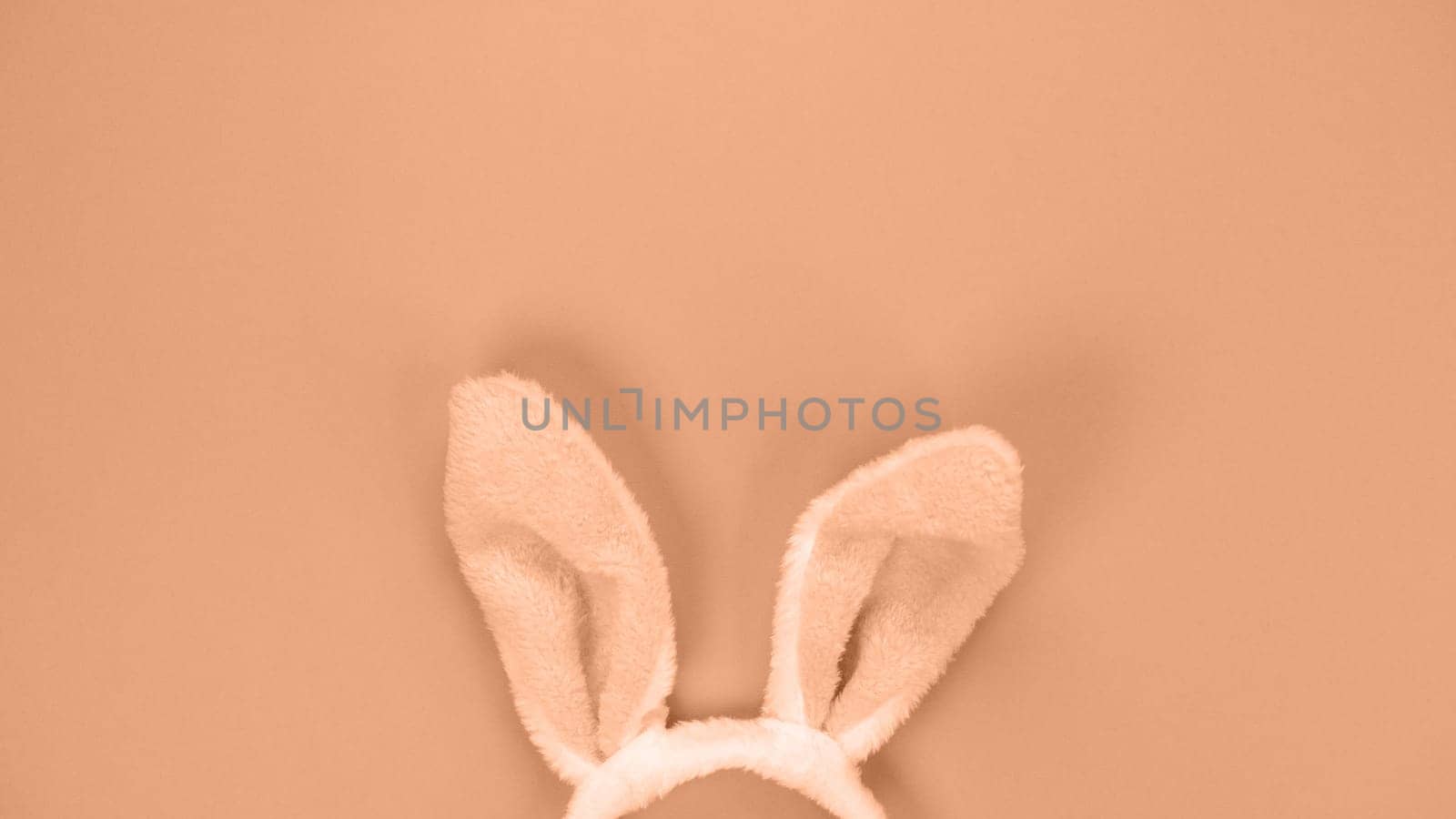 Decorative bunny ears furry fluffy costume toy. Image toned in Peach Fuzz color of the year 2024. Happy Easter concept. Simple minimalism flat lay top view copy space
