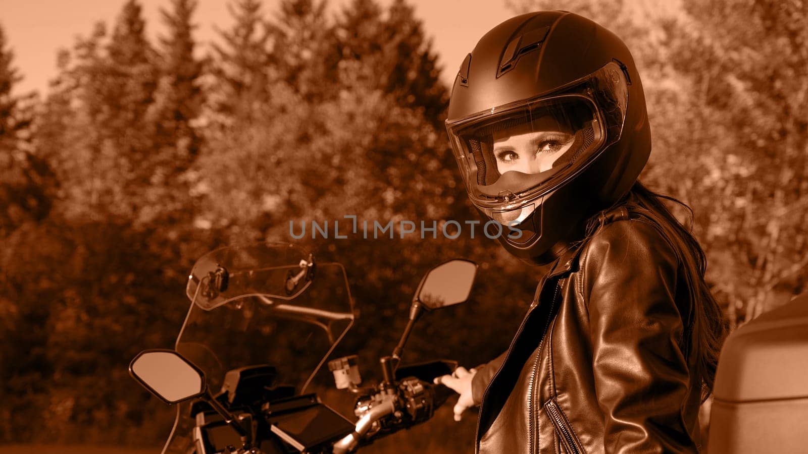 Biker girl riding touring motorbike on forest road. Image toned in Peach Fuzz color of the year 2024. Beautiful woman with red hair in leather jacket sitting on motorcycle in the park. by JuliaDorian