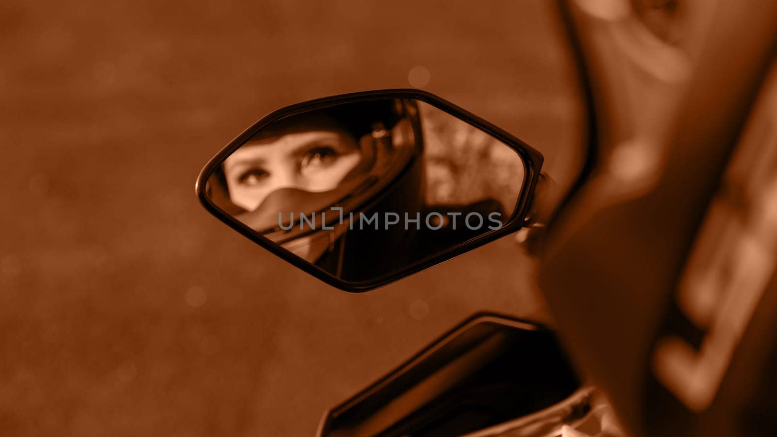 The girl on a motorcycle. Blurred reflection in mirror. Image toned in Peach Fuzz color of the year 2024. Selective focus. Displaying girls in the mirror of the motorcycle. Very beautiful eyes