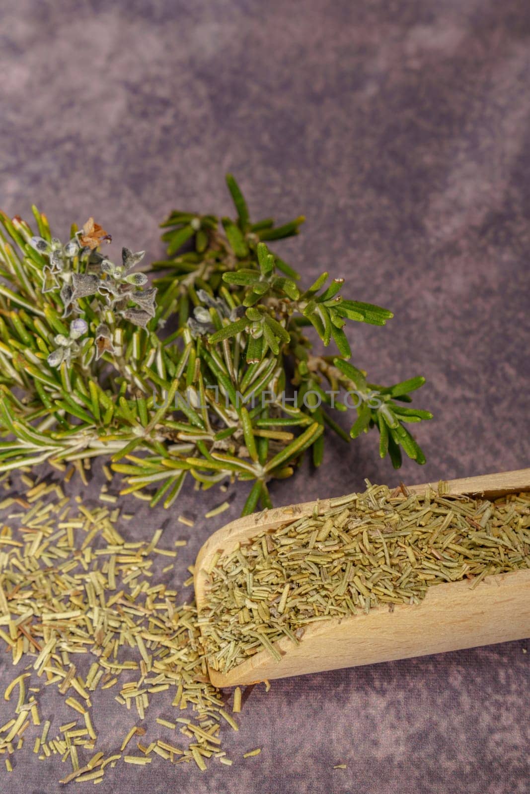 dried rosemary ground in a wooden spoon together with a branch of fresh rosemary blossoms