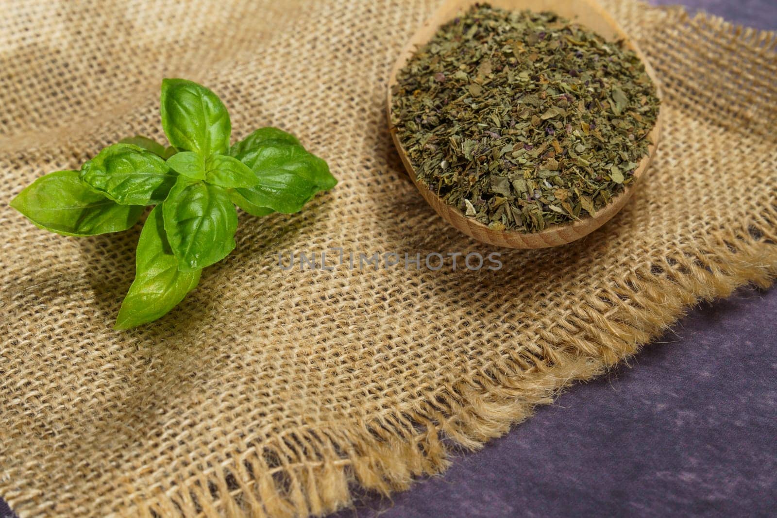 dried basil ground in a wooden spoon with freshly cut basil leaves on a burlap cloth