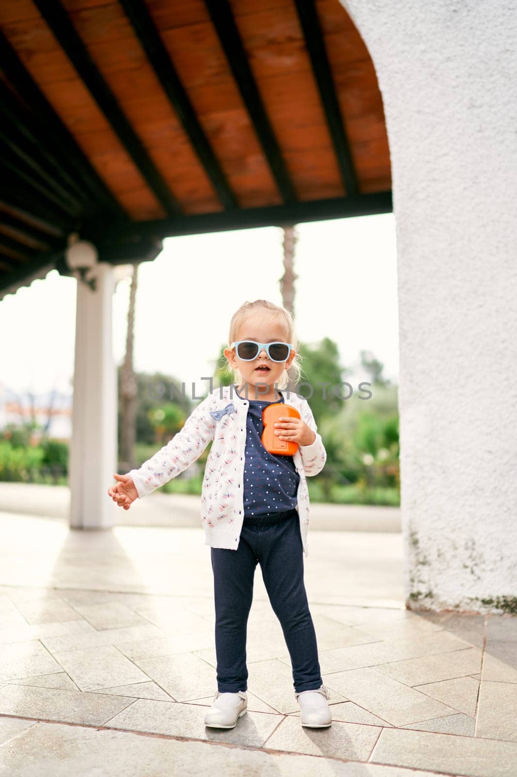 Little girl in sunglasses stands on a tile in a pergola in the garden. High quality photo