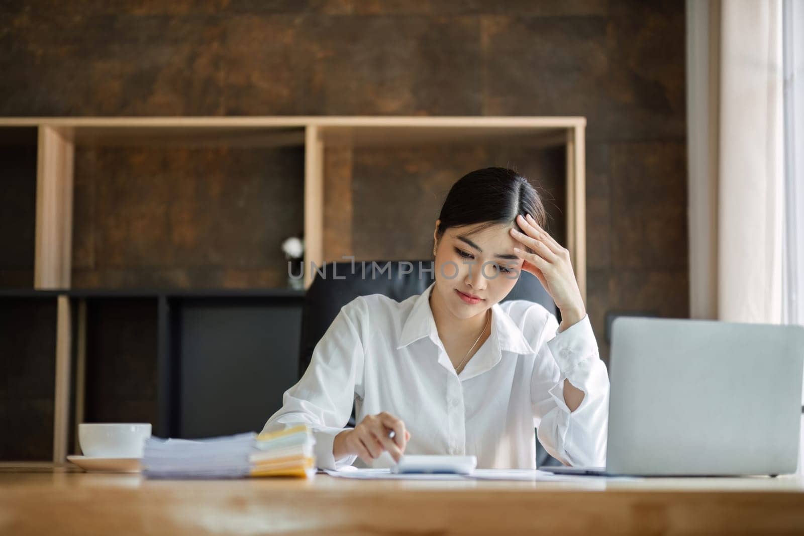 Young Asian business woman is having trouble controlling her online work in front of a laptop screen. Serious Asian businesswoman worried about solving work problems on computer.