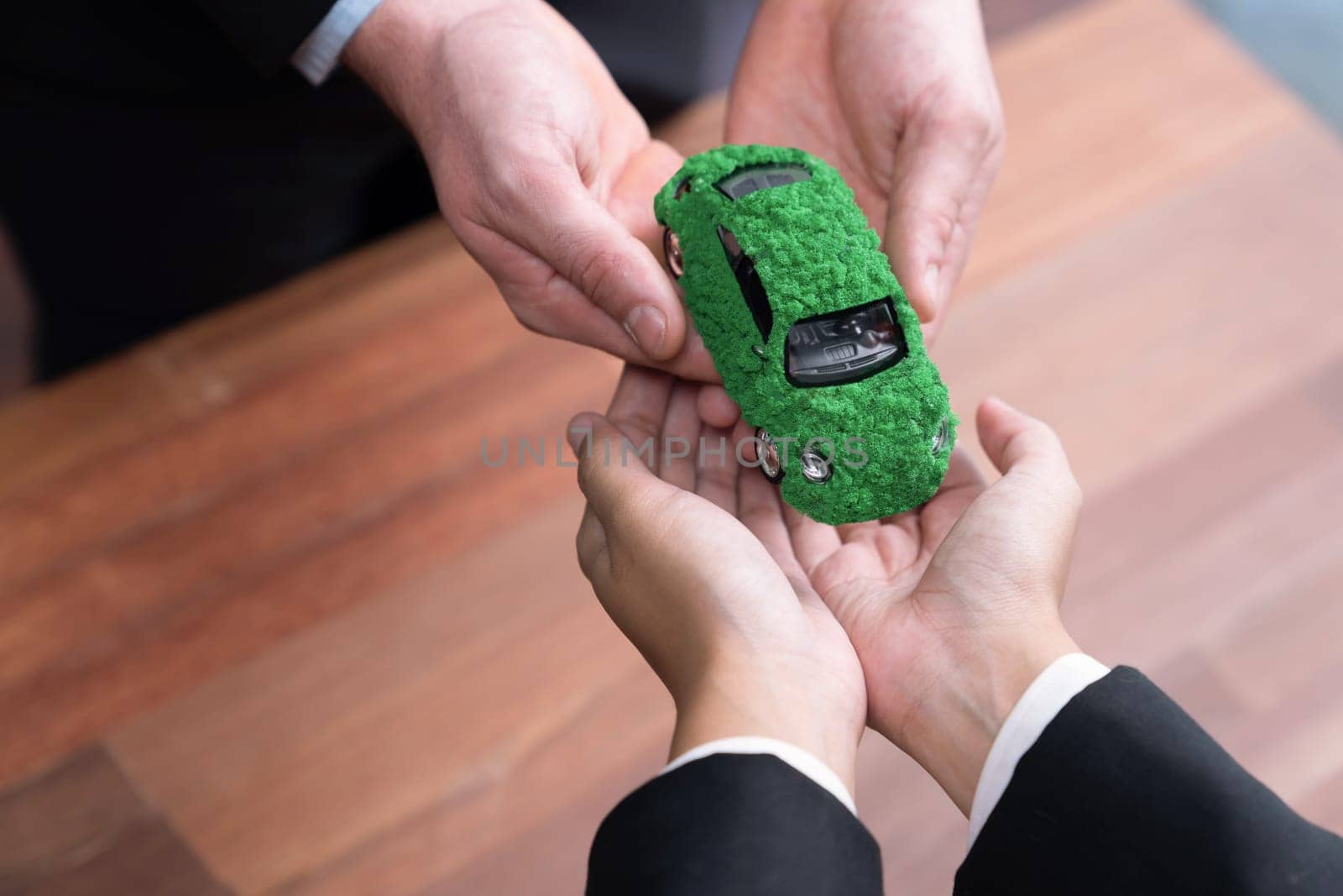 Business people exchange and holding green eco car model. Electric vehicle utilized by eco-friendly company for environmental friendly transportation. Zero CO2 emission corporate responsible. Quaint