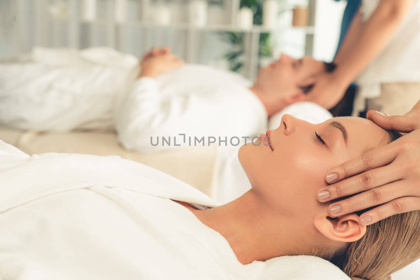Caucasian couple enjoying relaxing anti-stress head massage and pampering facial beauty skin recreation leisure in dayspa modern light ambient at luxury resort or hotel spa salon. Quiescent