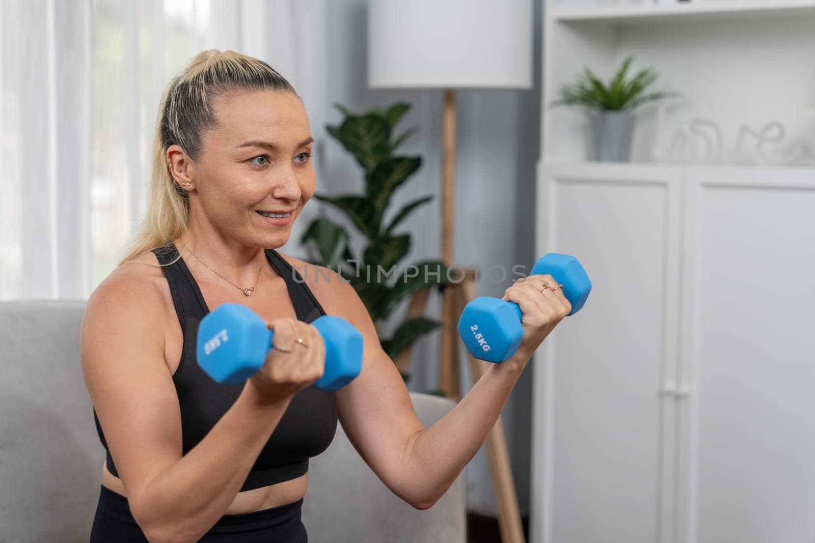Athletic and sporty senior woman lifting dumbbell at home. Clout by biancoblue