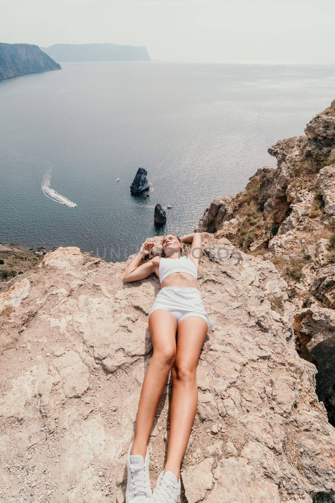 Woman travel sea. Happy tourist in hat enjoy taking picture outdoors for memories. Woman traveler posing on the beach at sea surrounded by volcanic mountains, sharing travel adventure journey