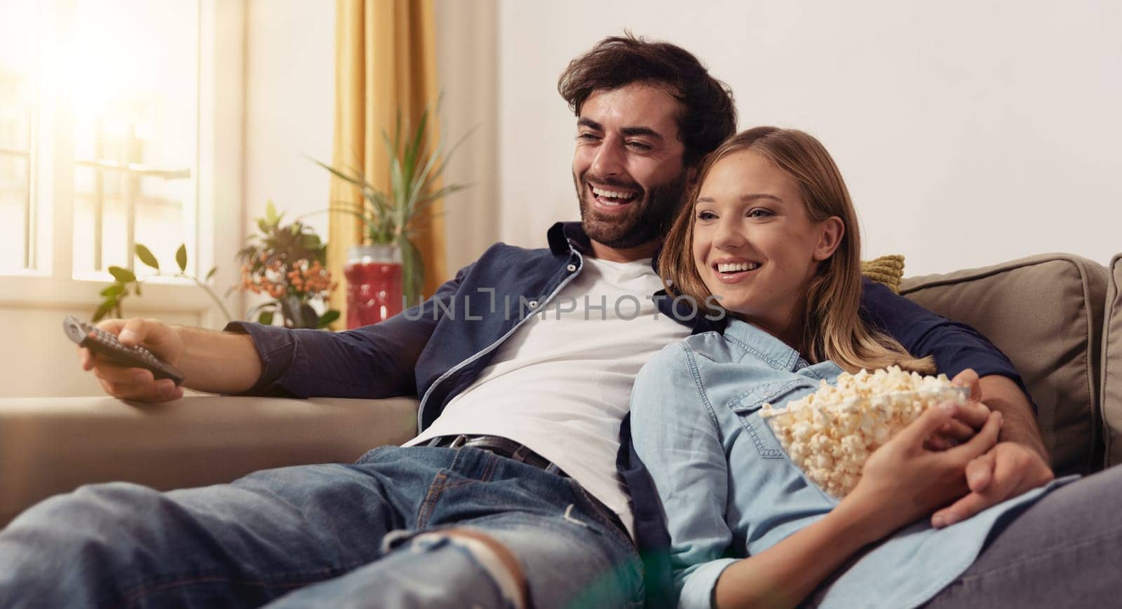 Couple watching TV, eating popcorn on a sofa at home