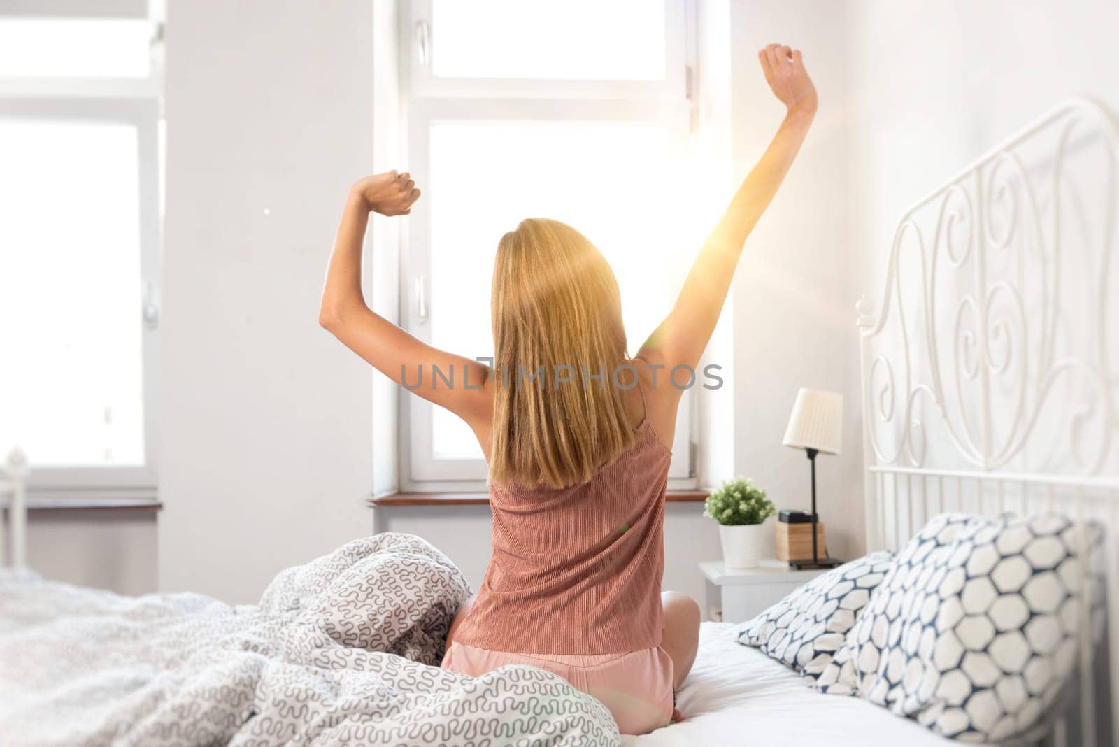 Back view of woman stretching in bed. Wake up at sunrise