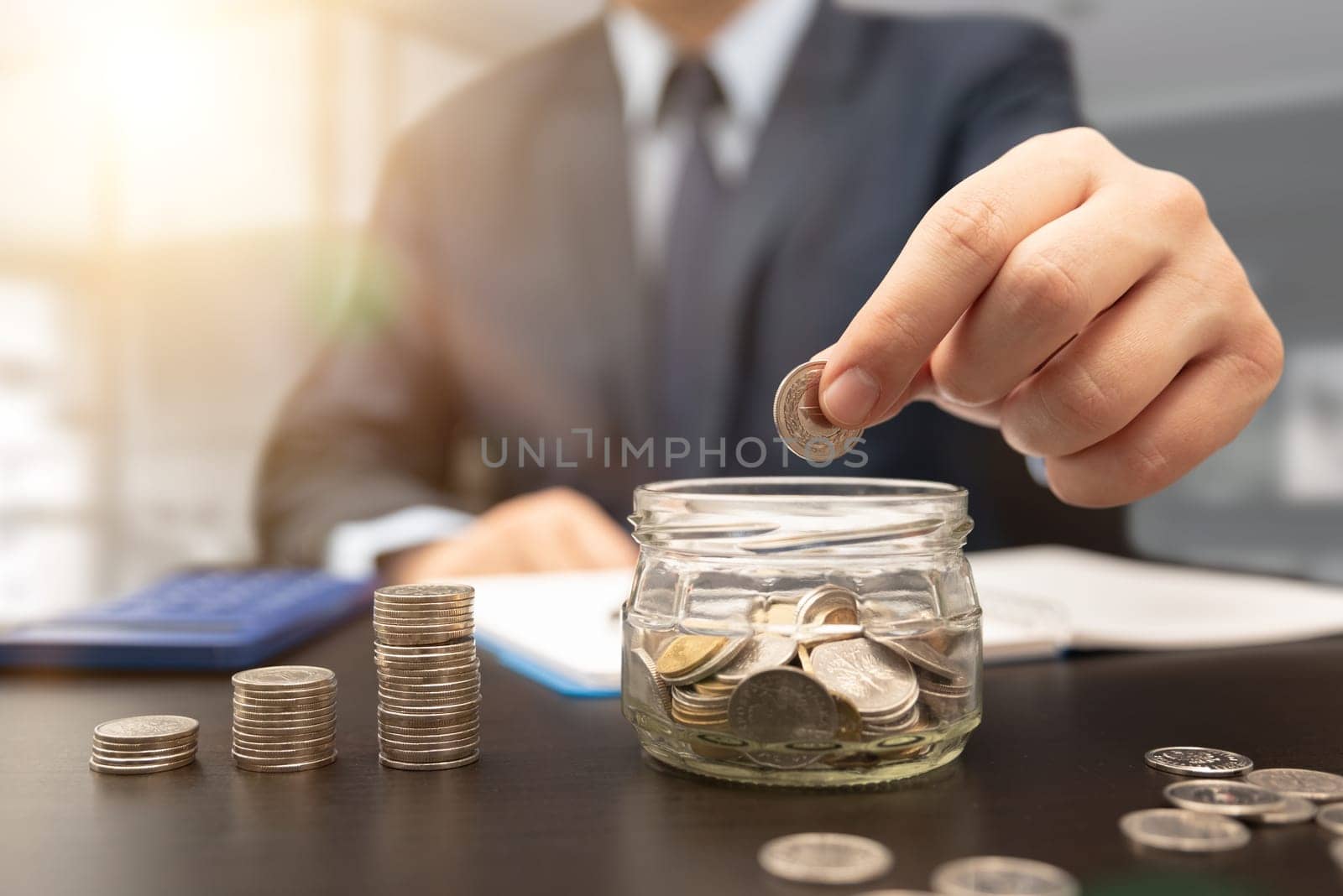 Man calculates the savings. Budget planning concept. Businessman working in the office. Man puts coins into the jar