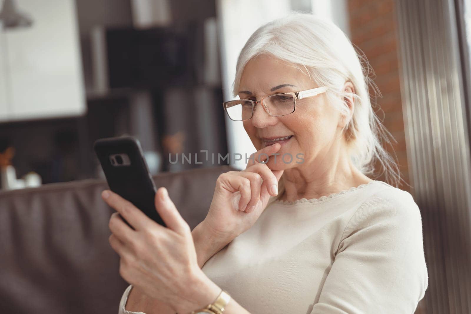 Beautiful senior woman texting at home. The pensioner uses social media