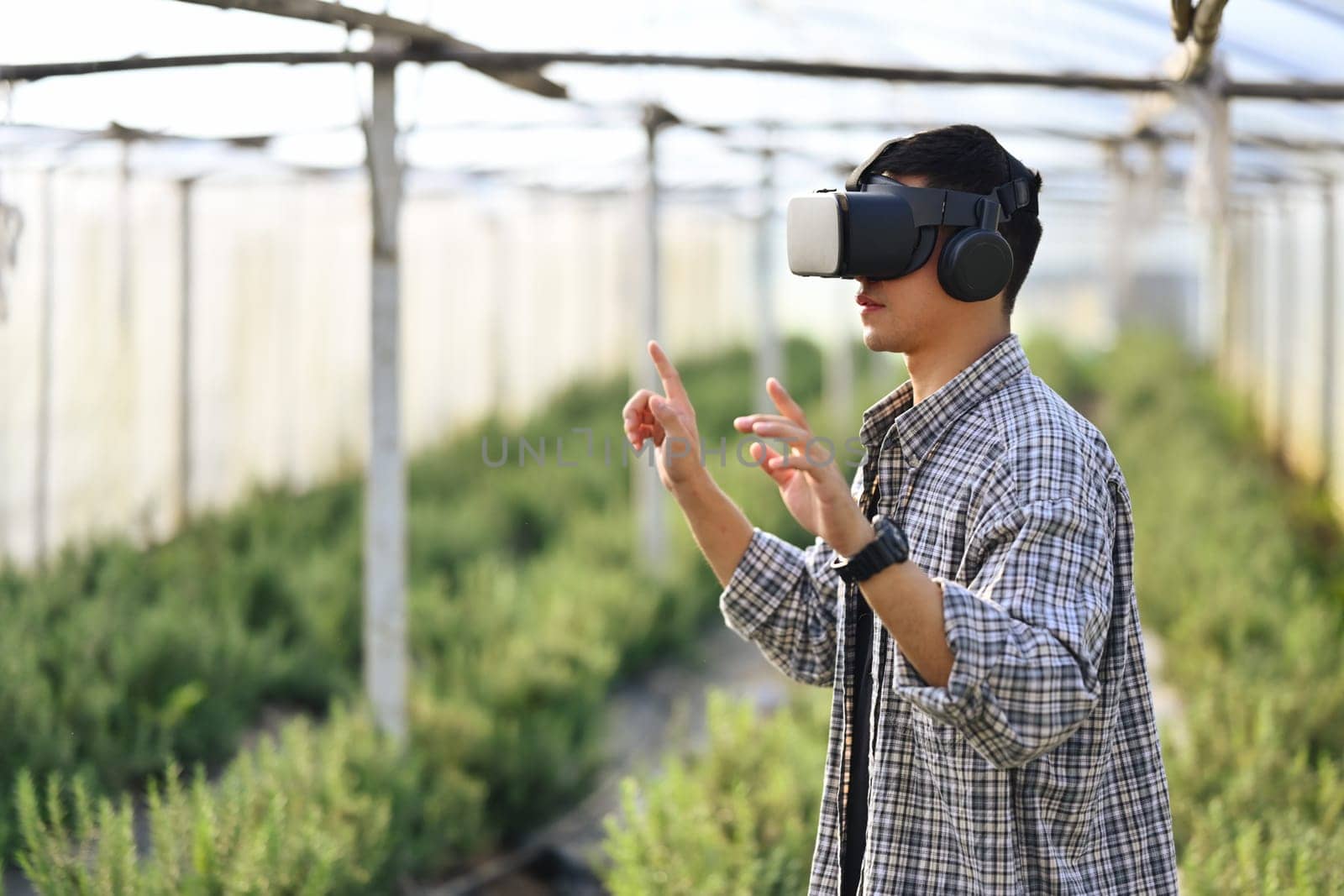 Farmer in VR headset controlling process of growing rosemary in greenhouse cultivation. Smart farming concept.