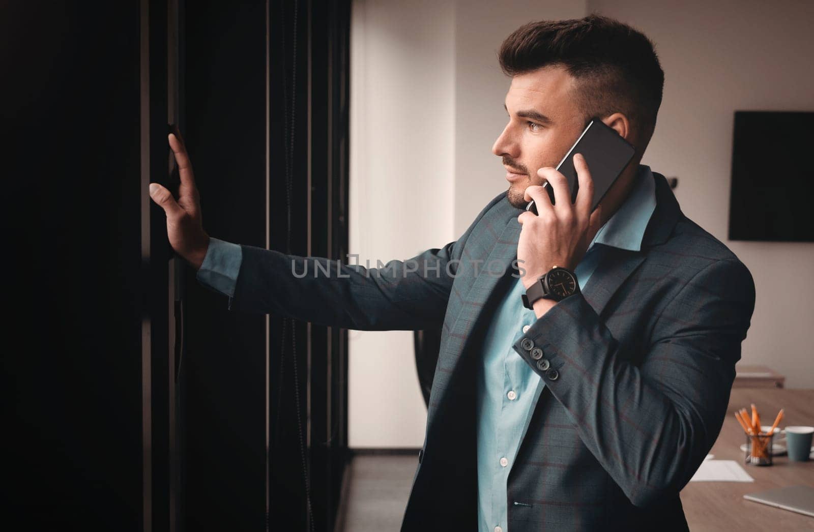 Portrait of a businessman in the office. Handsome man is standing by the window with phone