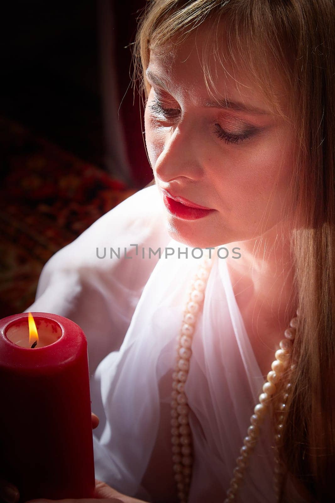 Beautiful arabian girl with candles in red room full of rich fabrics and carpets in sultan harem. Photo shoot of woman an oriental style odalisque. Model poses in sari as a caring wife and hostess by keleny