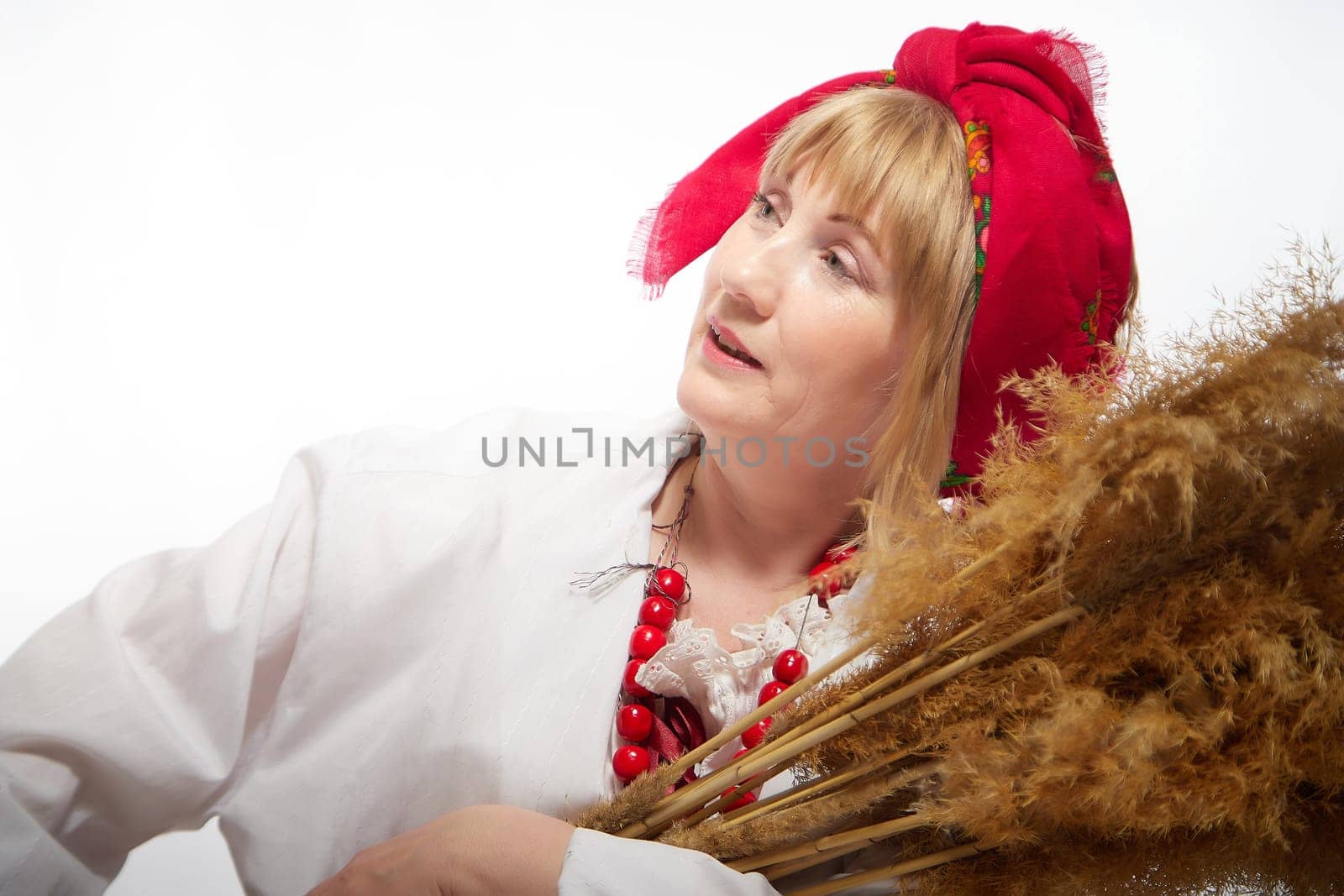 Portrait of heerful funny adult mature woman solokha with sheaf of ears. Female model in national ethnic Slavic style. Stylized Ukrainian, Belarusian or Russian woman in comic photo shoot