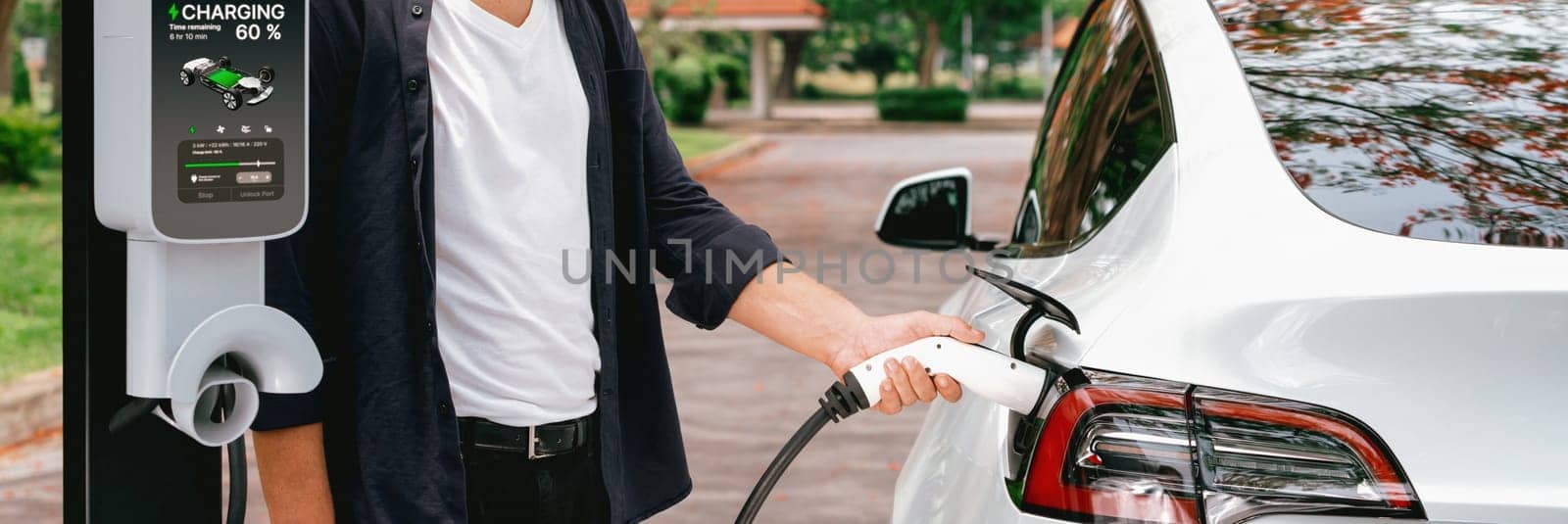 Panorama banner man recharging battery for electric car during autumnal road trip travel EV car in autumnal forest. Eco friendly travel on vacation during autumn with electric vehicle. Exalt