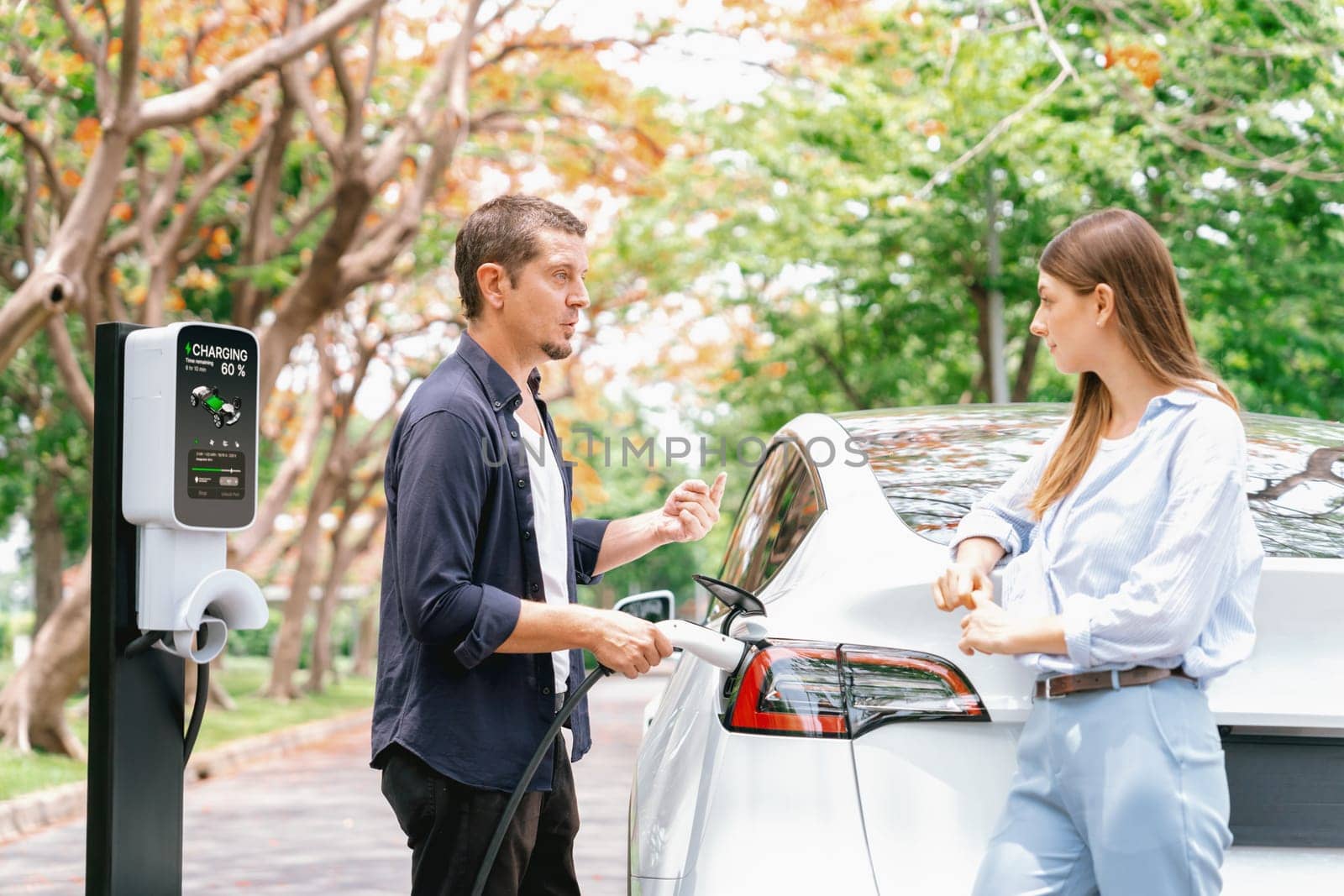 Lovely young couple recharging battery for electric car during autumnal road trip travel EV car in autumnal forest. Eco friendly travel on vacation during autumn. Exalt