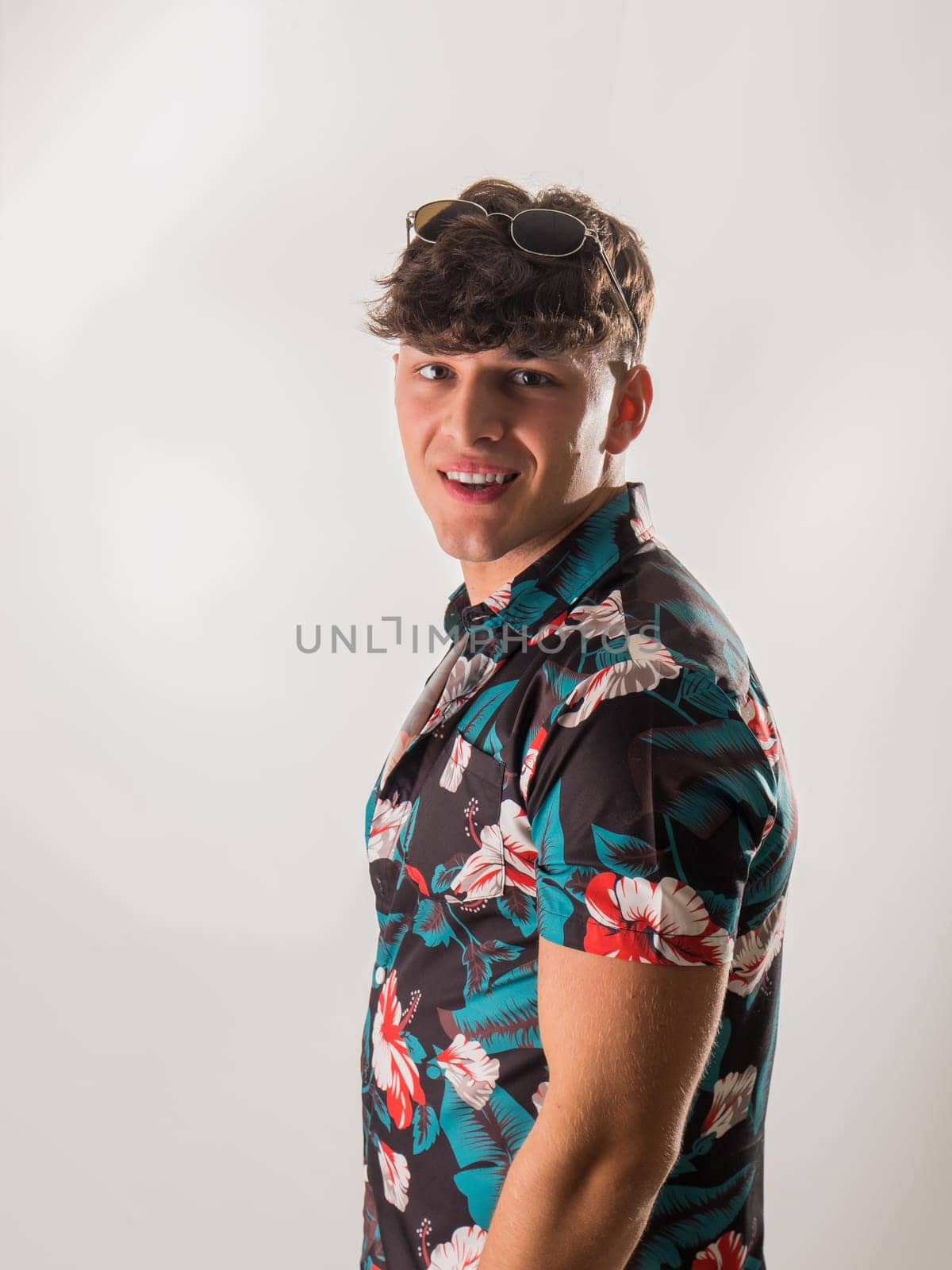 Attractive, muscular young man smiling, wearing open hawaian style shirt on white background