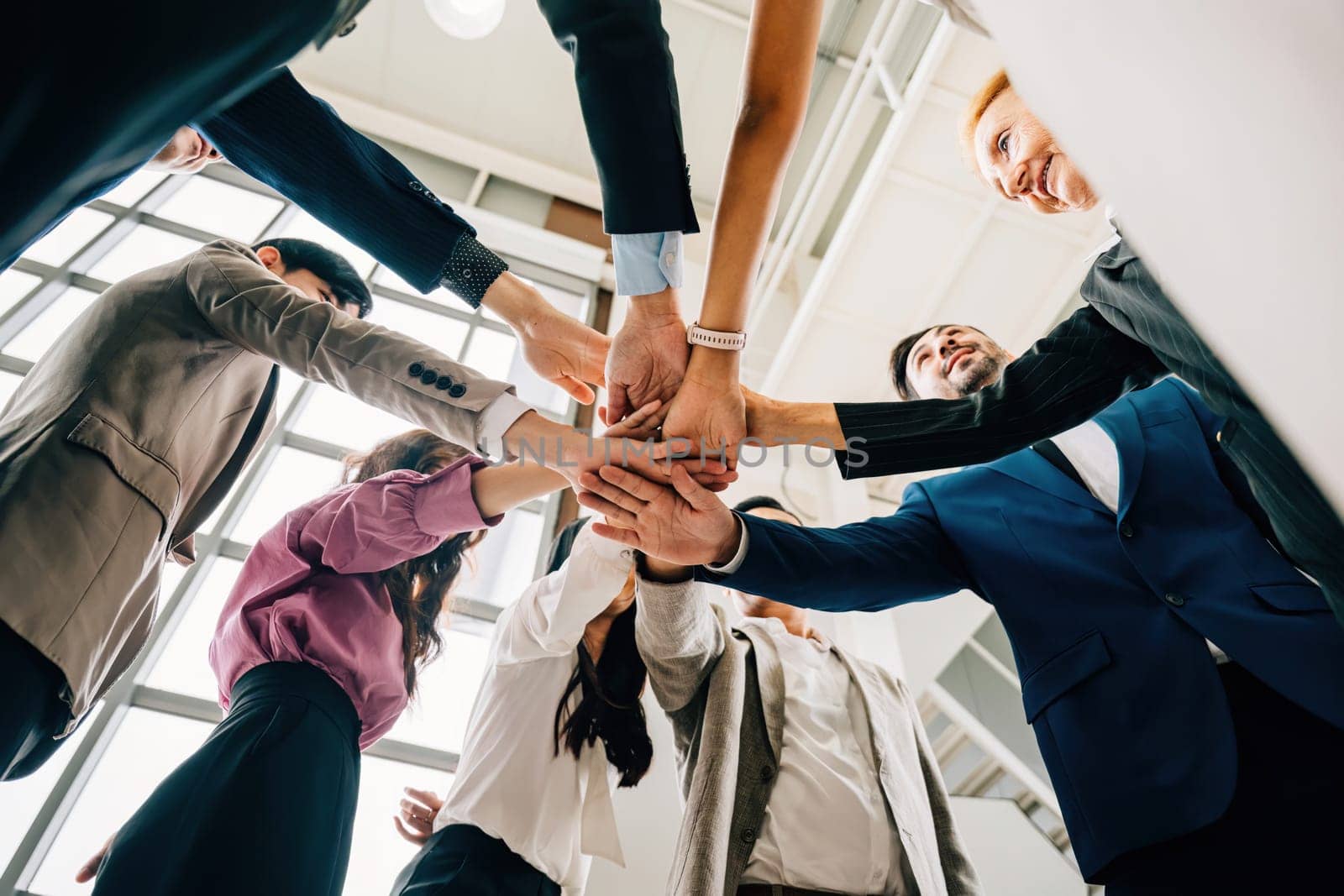 An under shot captures four diverse business colleagues in a unity circle stacking their hands. This symbolizes teamwork success and global cooperation in the corporate world by Sorapop