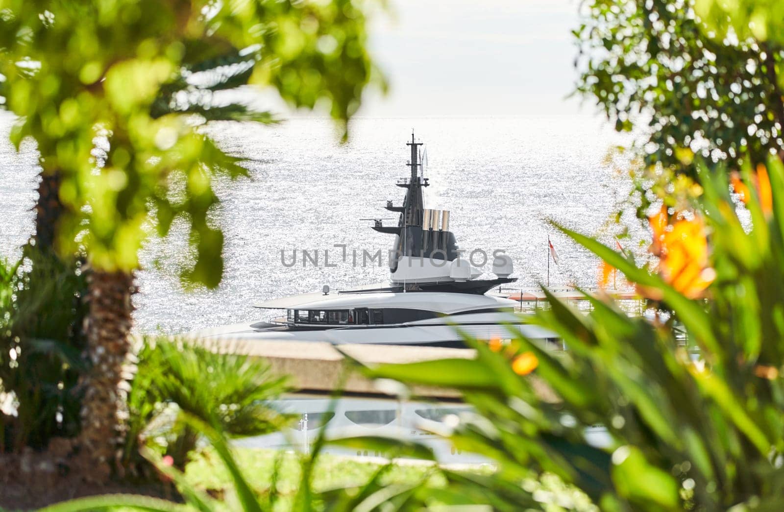 Monaco, Monte Carlo, 27 September 2022 - top of huge luxury yacht through trees and flowers at sunny day, the famous motorboat exhibition in the principality. High quality photo