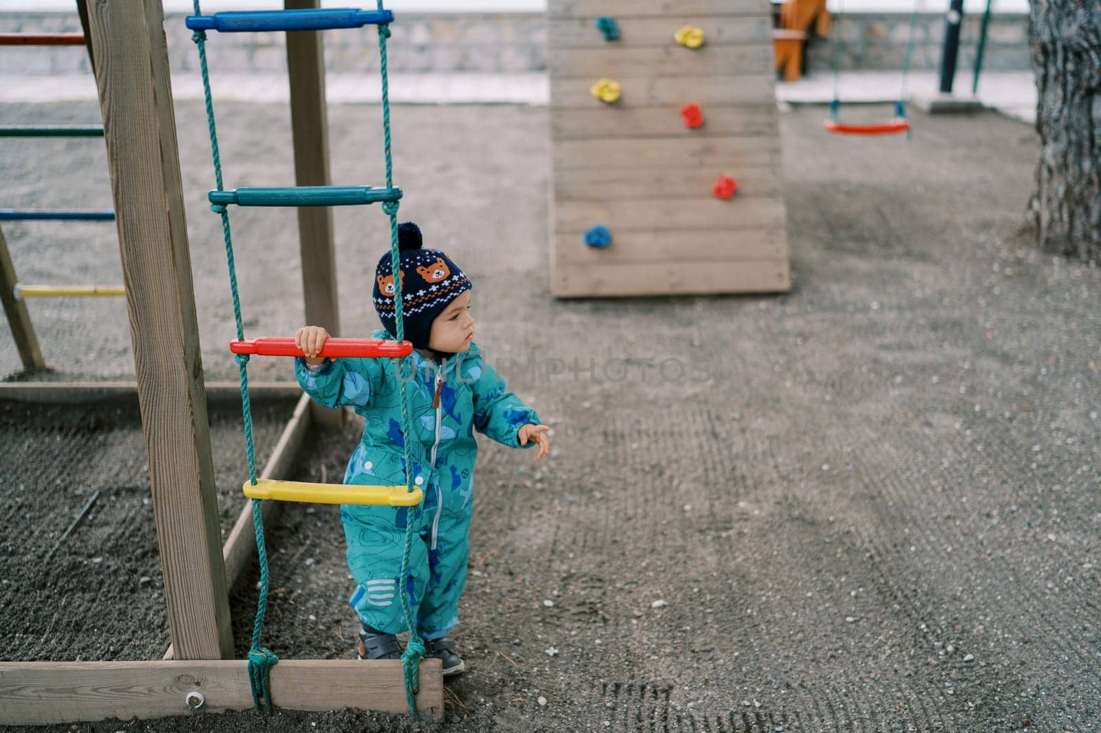 Little girl stands near a rope ladder and looks away by Nadtochiy