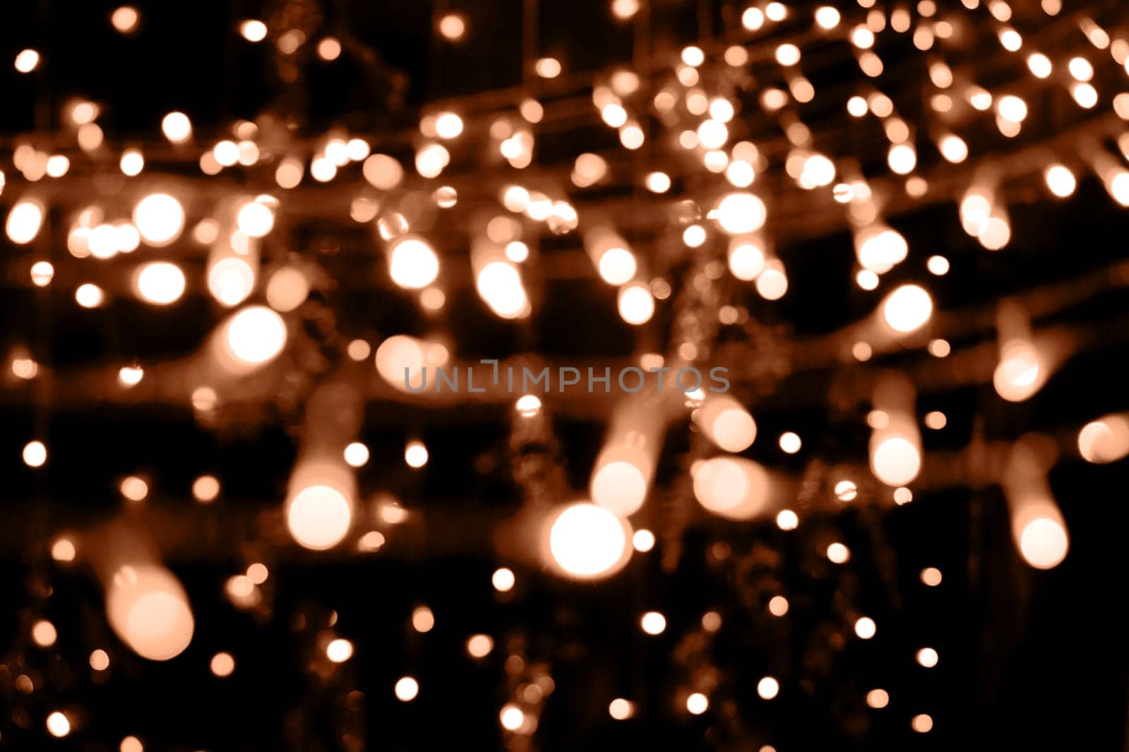 Blurry garland lights on a dark background. Festive Christmas and New Year background. Soft focus. Image toned in color of the year 2024 - Peach Fuzz.