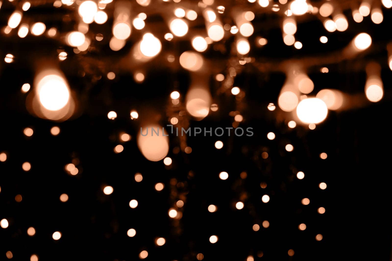 Blurry garland lights on a dark background. Festive Christmas and New Year background. Soft focus. Image toned in color of the year 2024 - Peach Fuzz by Annu1tochka