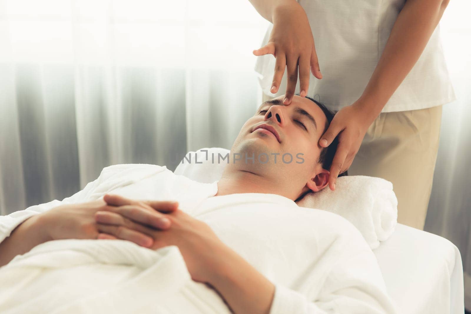 Caucasian man enjoying relaxing anti-stress head massage and pampering facial beauty skin recreation leisure in dayspa modern light ambient at luxury resort or hotel spa salon. Quiescent