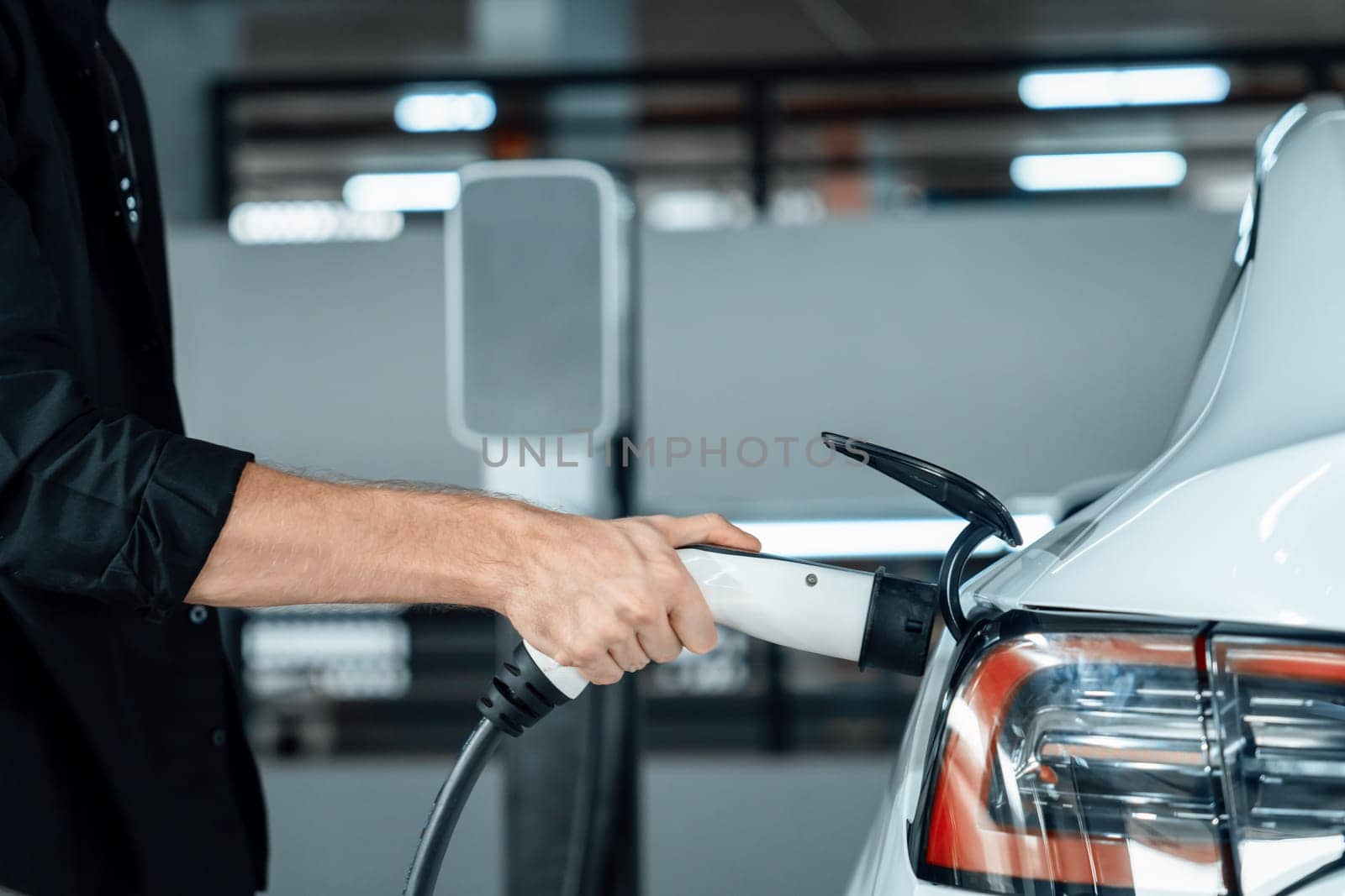 Young man travel with EV electric car to shopping center parking lot charging in downtown city showing urban sustainability lifestyle by green clean rechargeable energy of electric vehicle innards