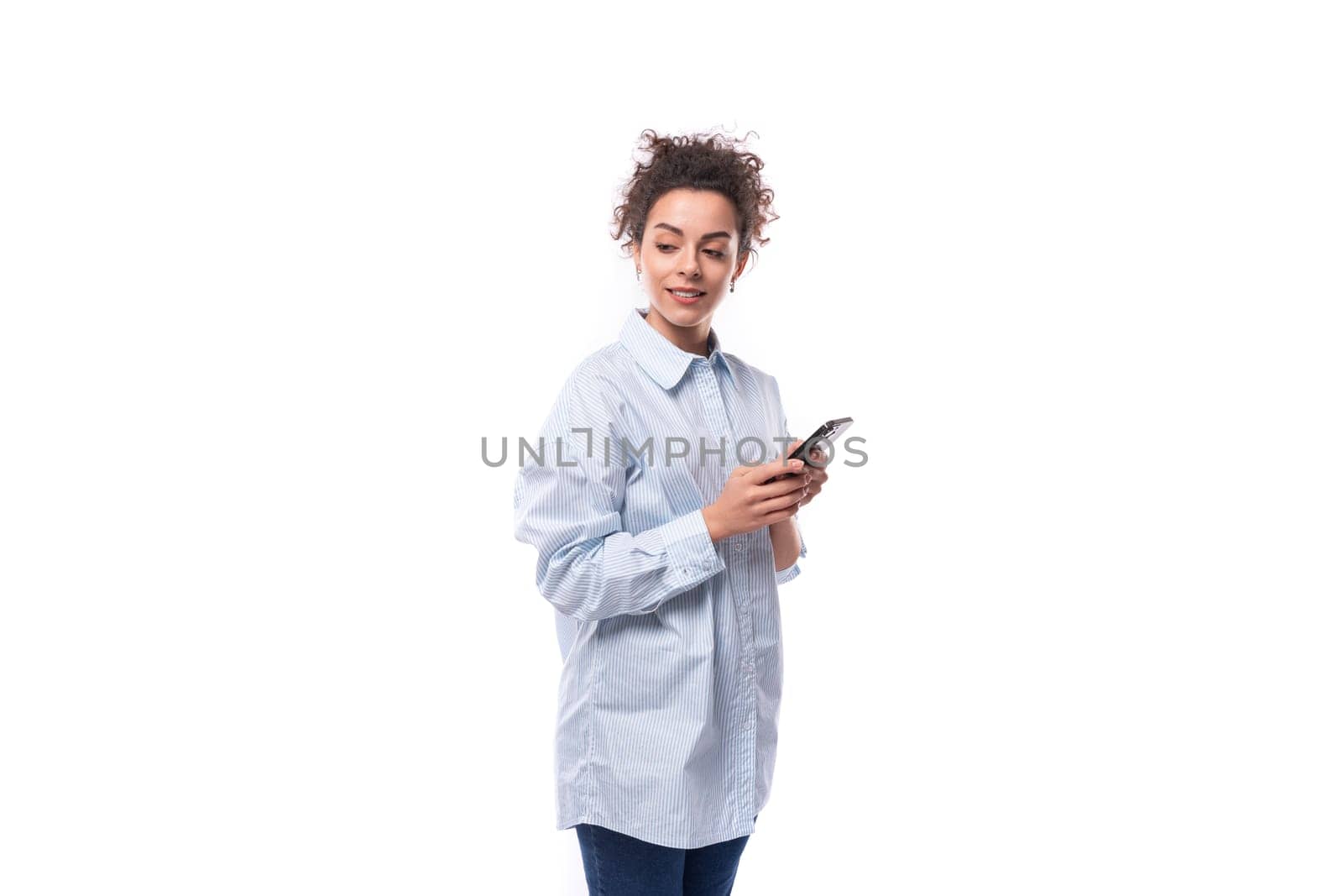 young pretty curly brunette secretary woman oeta in a light blue shirt writes a message on a mobile phone.