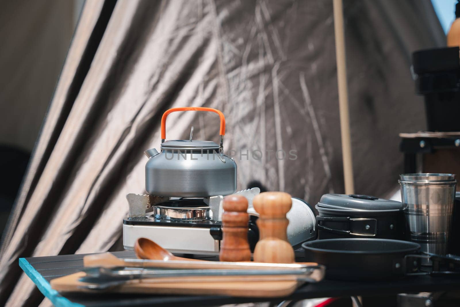 Campsite perfection, kettle, pot, pan, gas stove, flashlight, and camera neatly arranged at the front of the tent. Experience the joy of camping amidst nature's beauty.