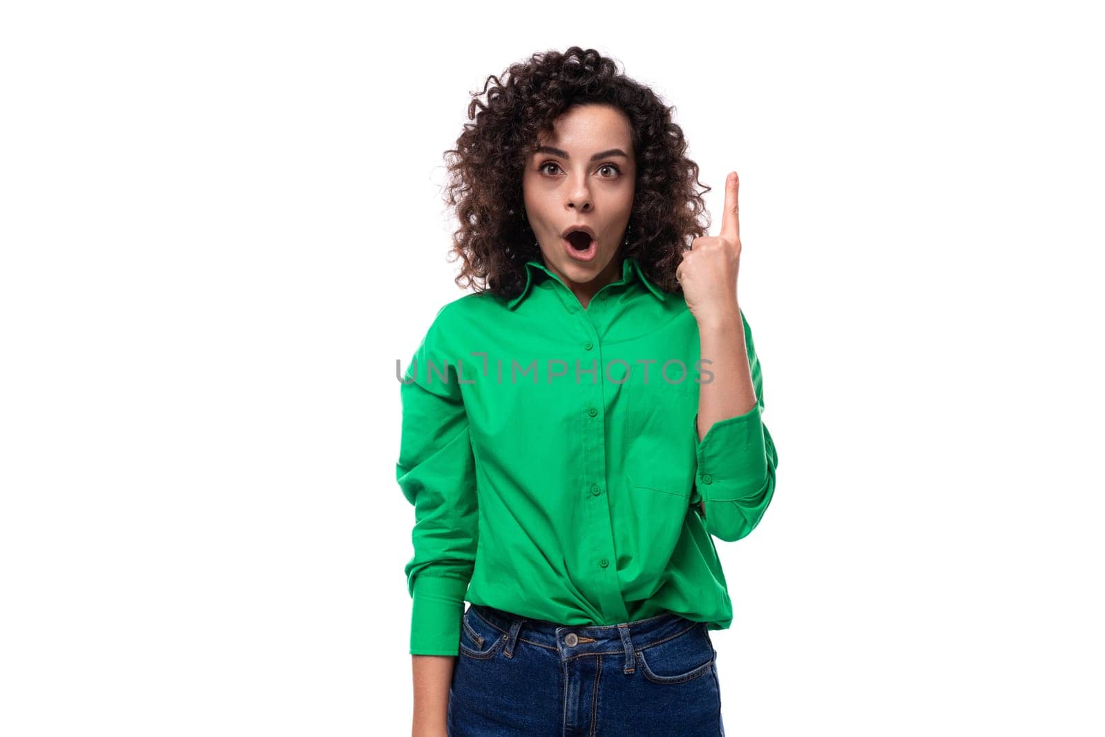 surprised young woman with black curly hair dressed in a green blouse points her fingers up.