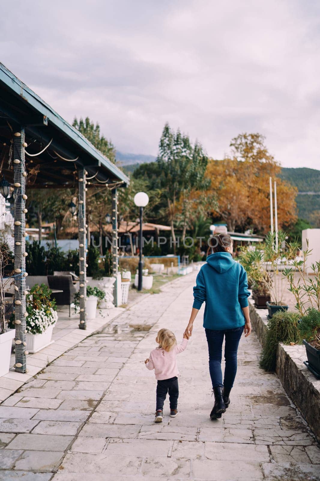Mother and little girl are walking down the street holding hands. Back view. High quality photo