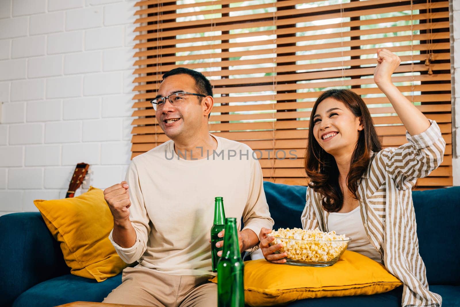 Excited young couple celebrates victory while watching TV their cheers filling the room with happiness by Sorapop