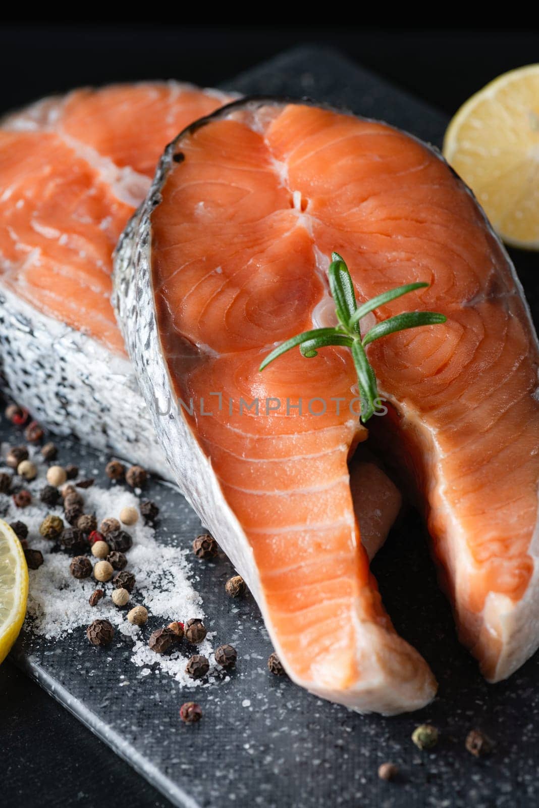 Raw salmon steak with lemon and herb on the dark background.