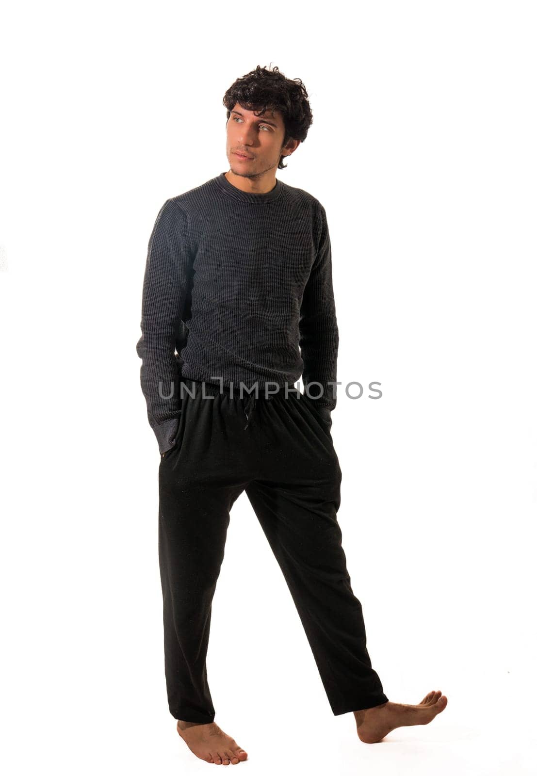 A man in a black sweater and black pants, walking around, with hands in pockets, full figure shot isolated on white