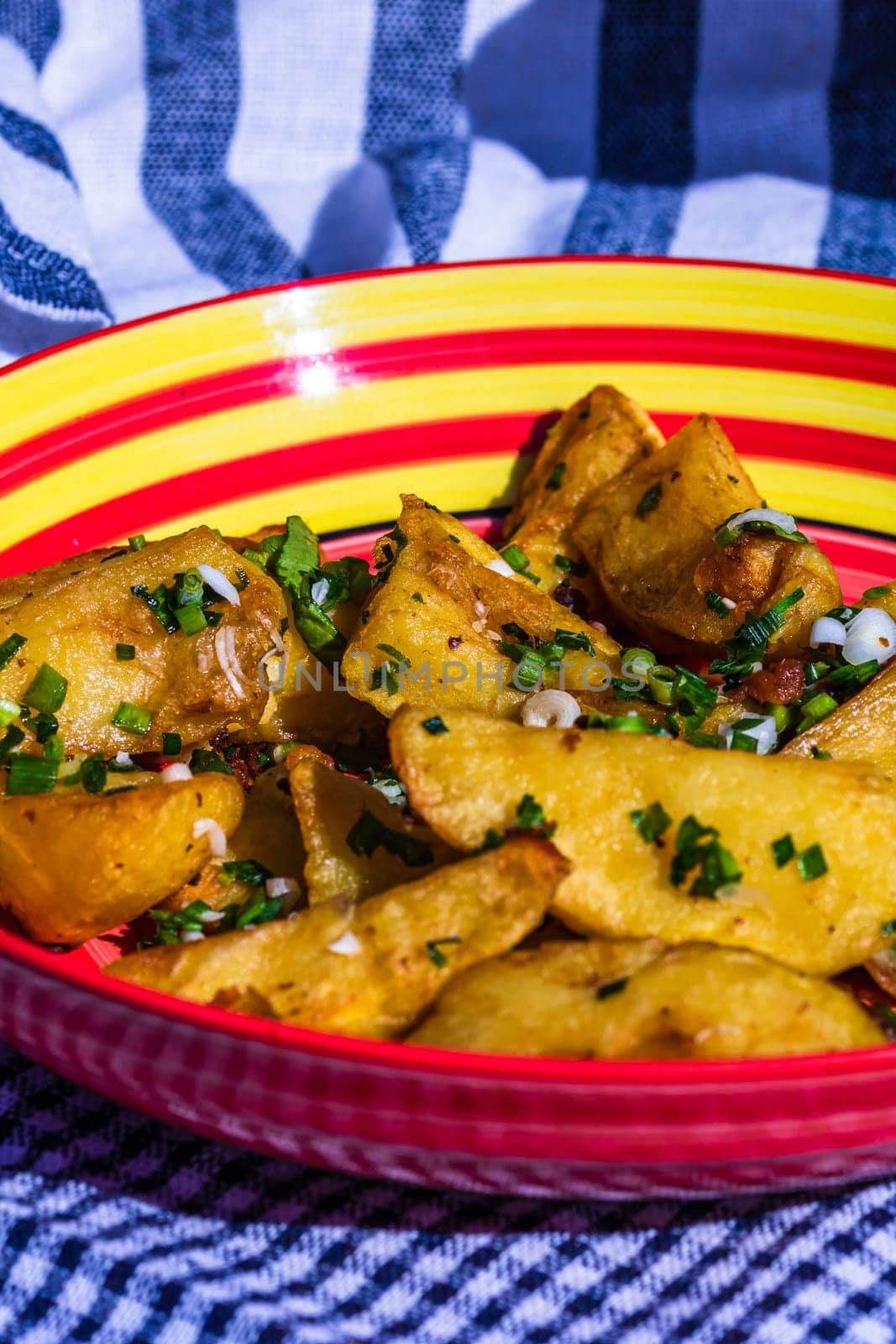 Close up with selective focus of fried potatoes with green onion, green garlic and spices in a colorful plate.