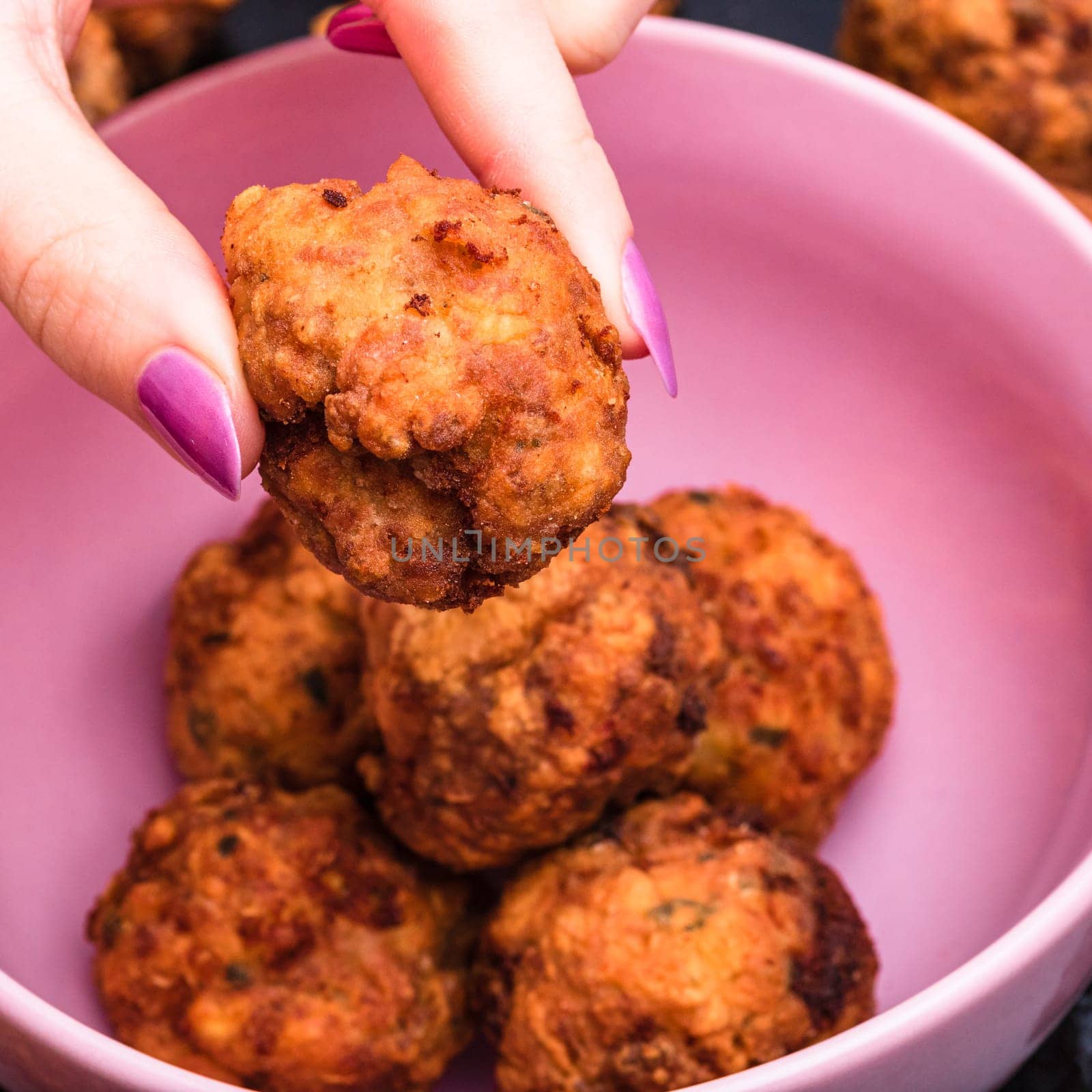 Pink bowl with fried meatballs with spices. Homemade food. Hand holding a fried meatball.