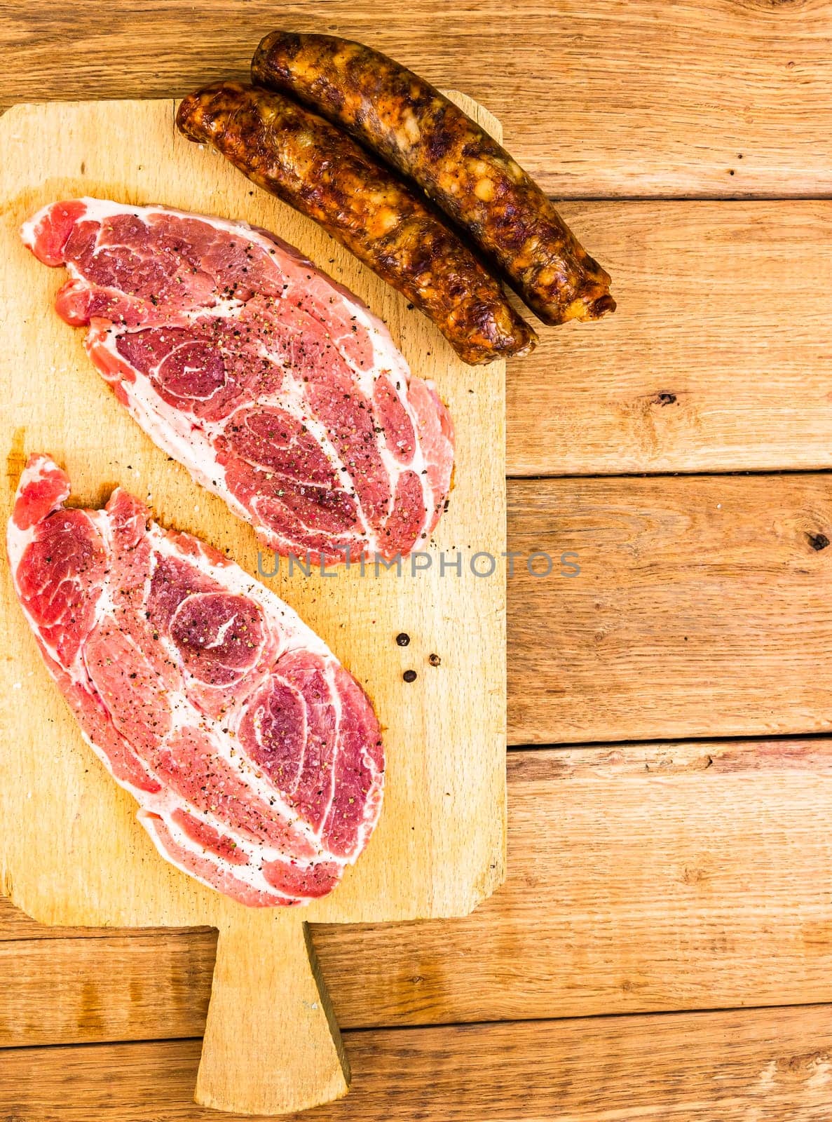 Pork chops with condiments and smoked sausage on a wooden cutting board over wooden table, meat for bbq, top view, copy space, barbeque concept by vladispas