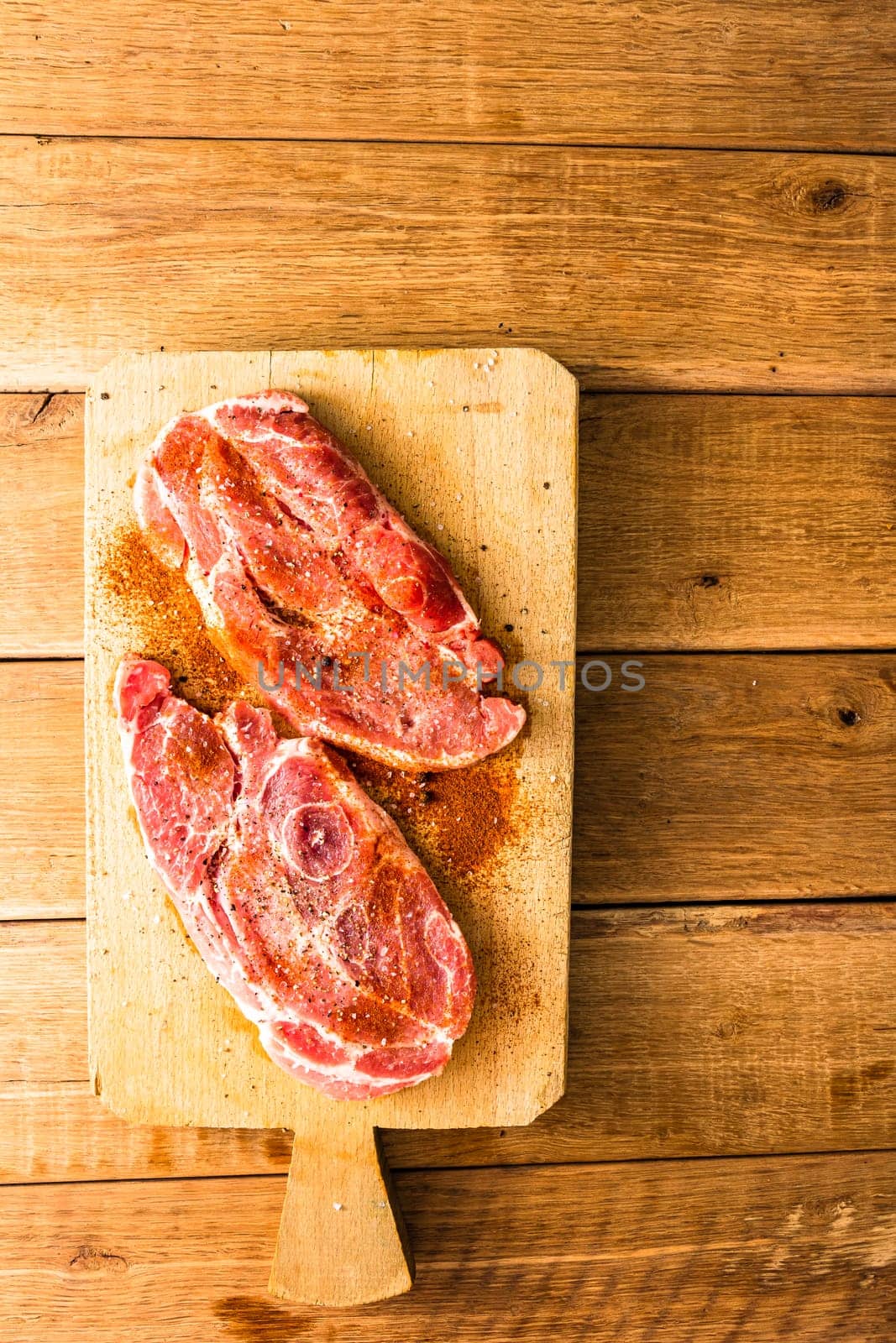 Pork chops with condiments on a wooden cutting board over wooden table, meat for bbq, top view, copy space, barbeque concept
