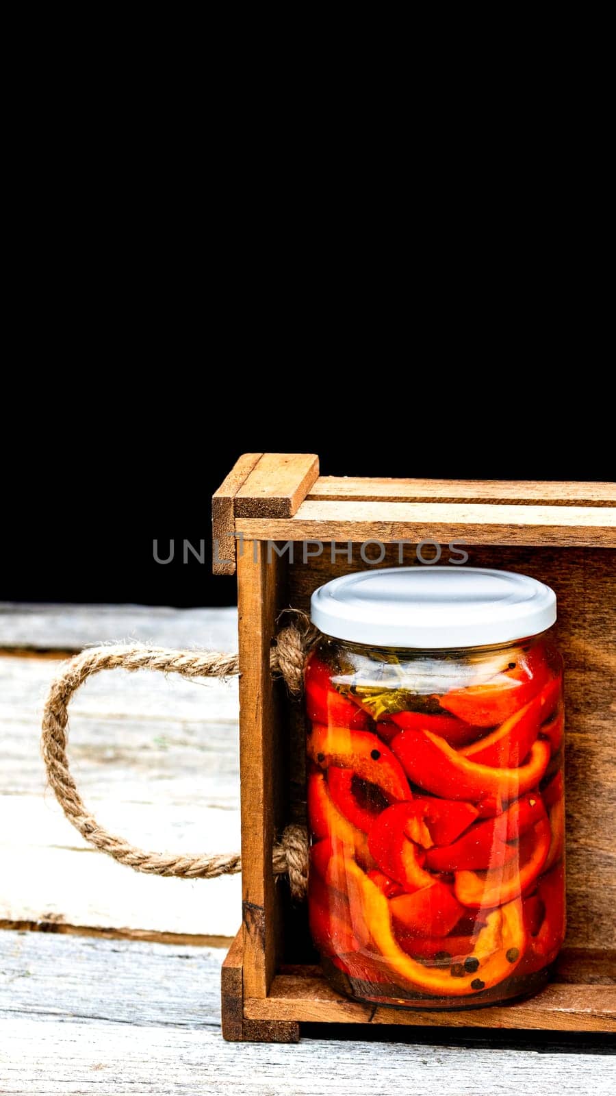 Wooden crate with glass jars with pickled red bell peppers.Preserved food concept, canned vegetables isolated in a rustic composition.