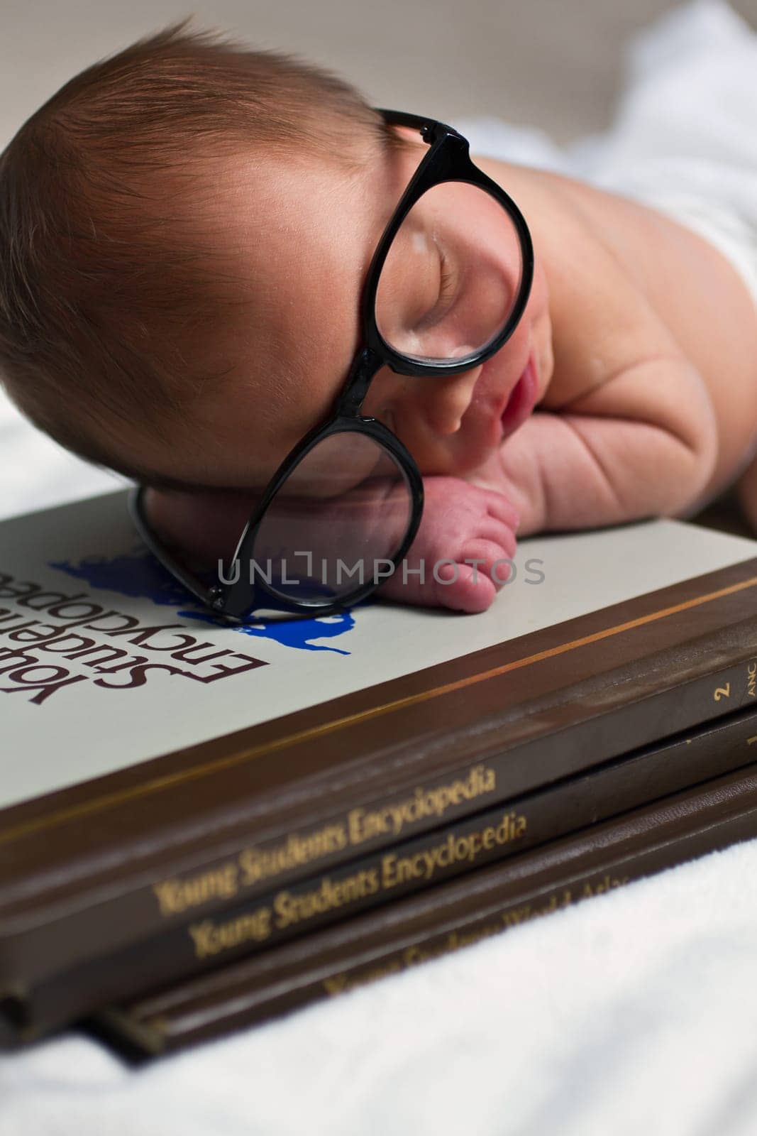 Infant Scholar: Newborn with Oversized Glasses on Stack of Encyclopedias by njproductions
