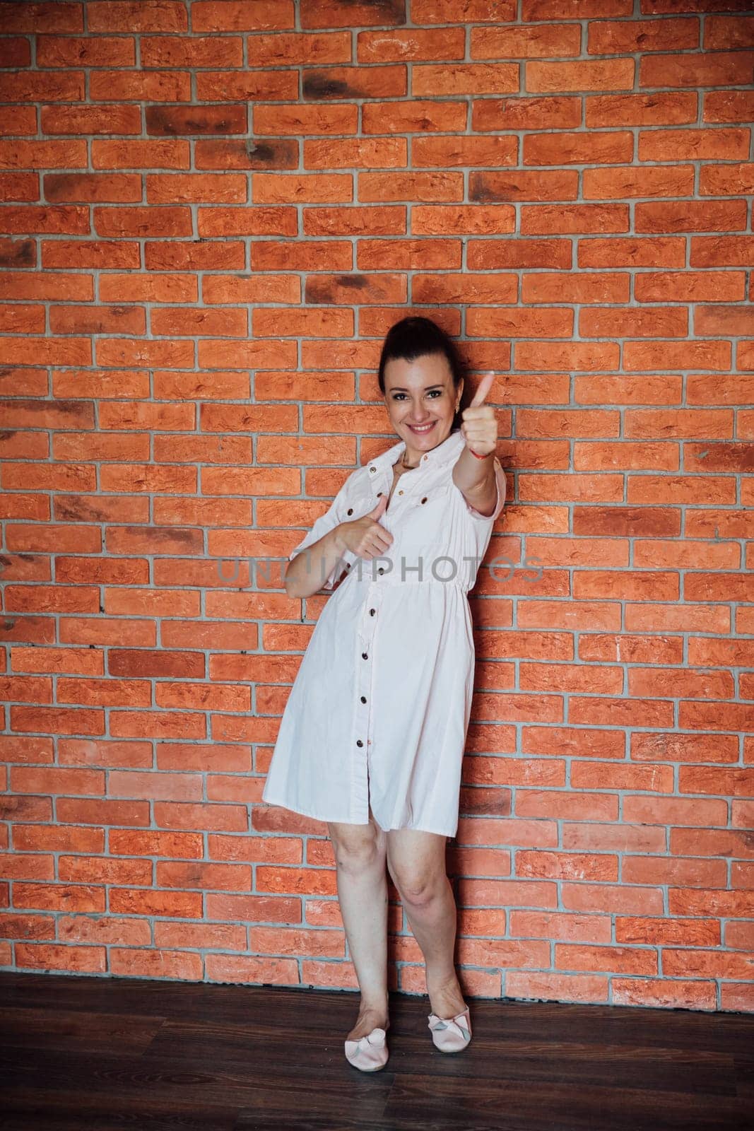 brunette woman in dress standing against brick wall