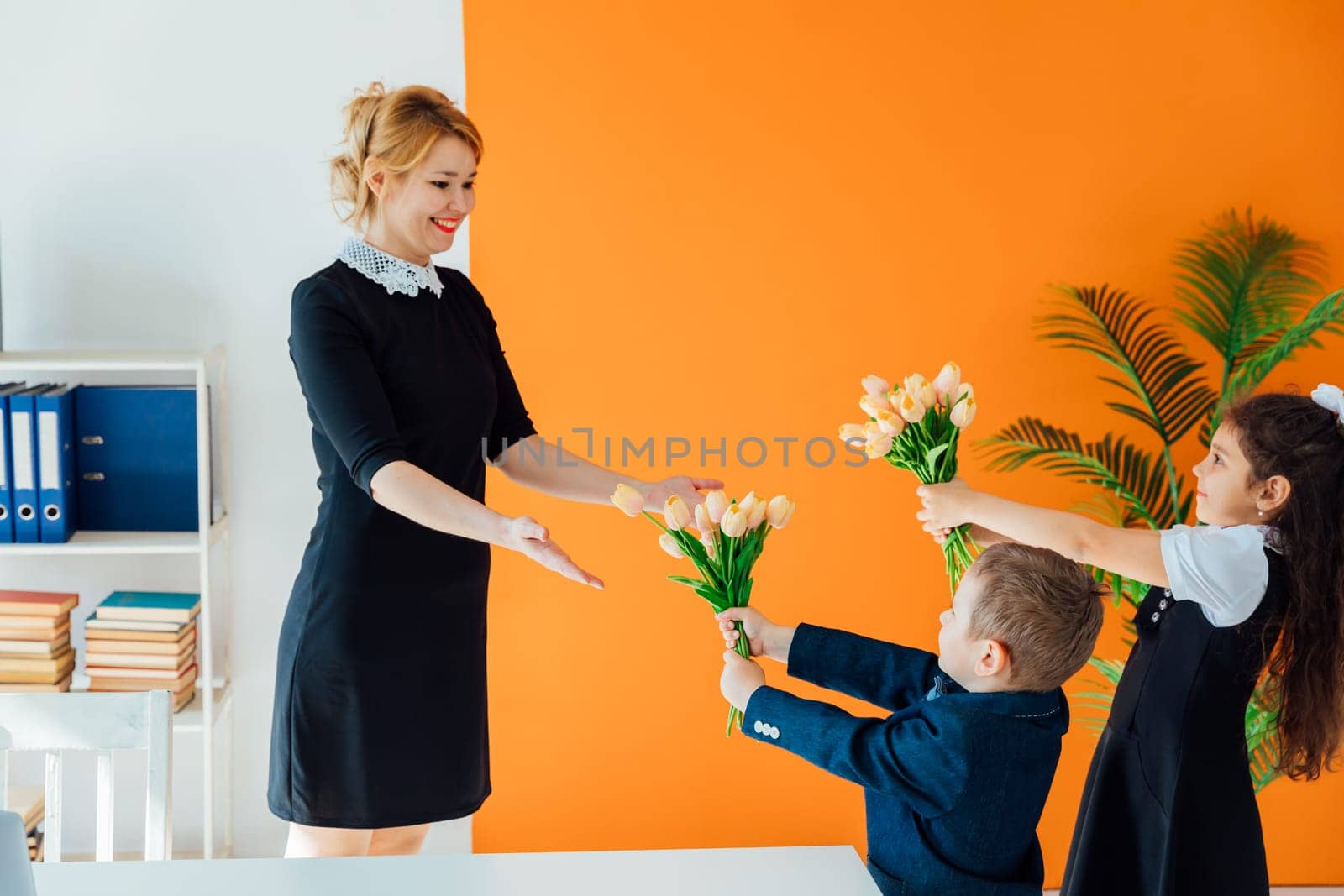 Schoolchildren giving flowers to teacher for holiday in classroom by Simakov