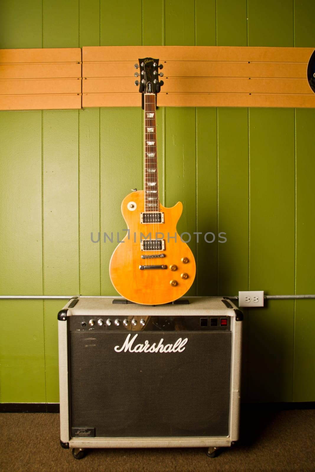 Rock and Roll Vibes: A sunburst electric guitar leans against a green wall, contrasting sharply and drawing attention to its sleek, polished body. The iconic Marshall amplifier stands ready for performance, evoking power and presence.