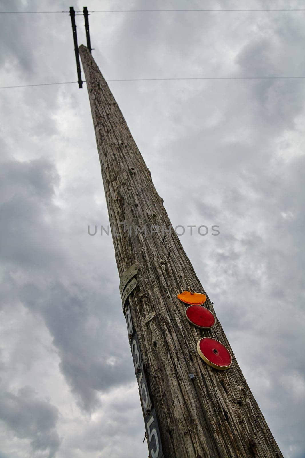 Rugged utility pole with reflective markers against cloudy sky, symbolizing connectivity and resilience in the face of natural forces. Perfect for industries related to infrastructure, telecommunications, and weathering adversity.
