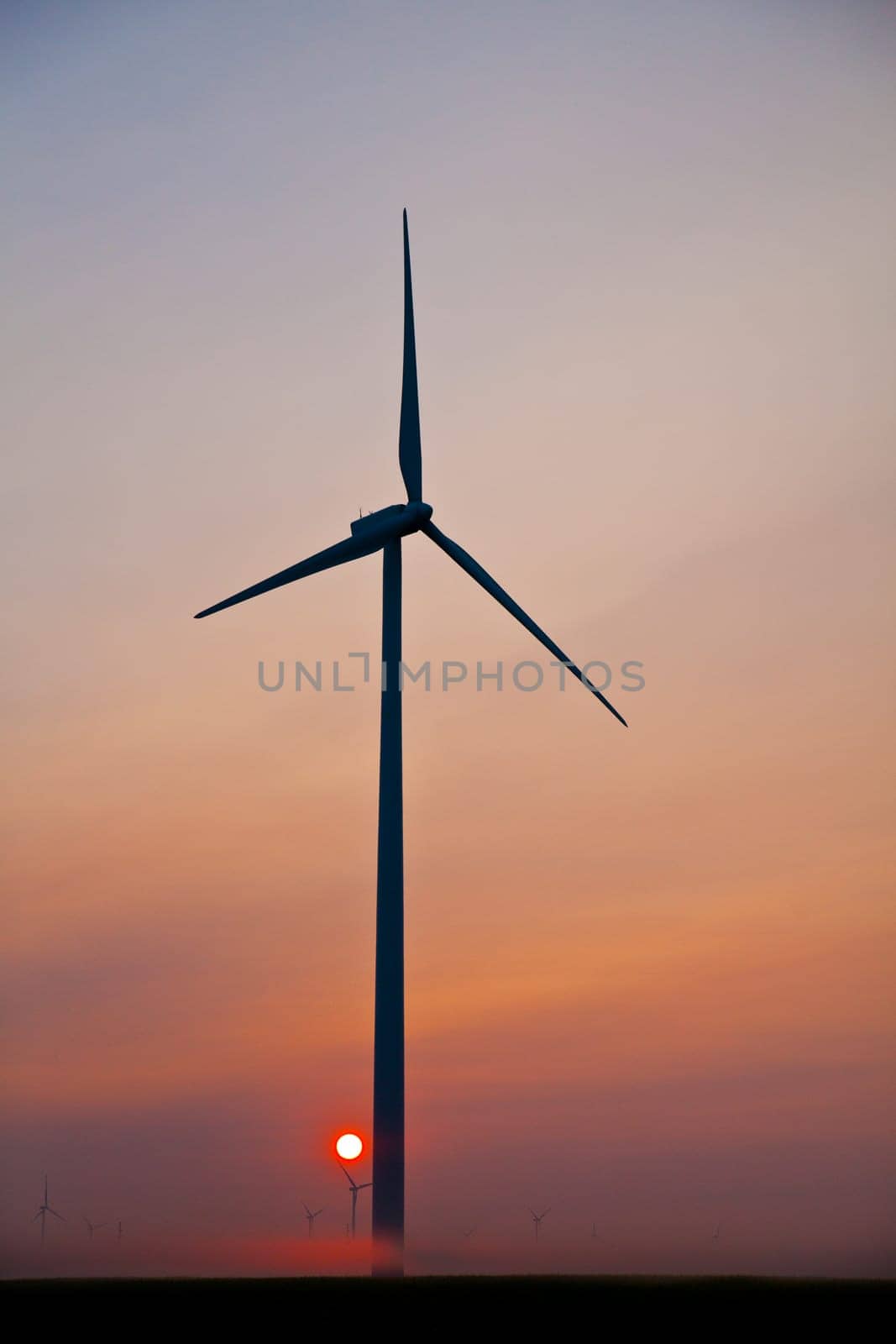 Sustainable Energy at Sunset: Majestic wind turbine cradles the sun, surrounded by a serene landscape dotted with distant turbines. A captivating image of renewable energy and harmonious integration with nature. Shot in Ohio.