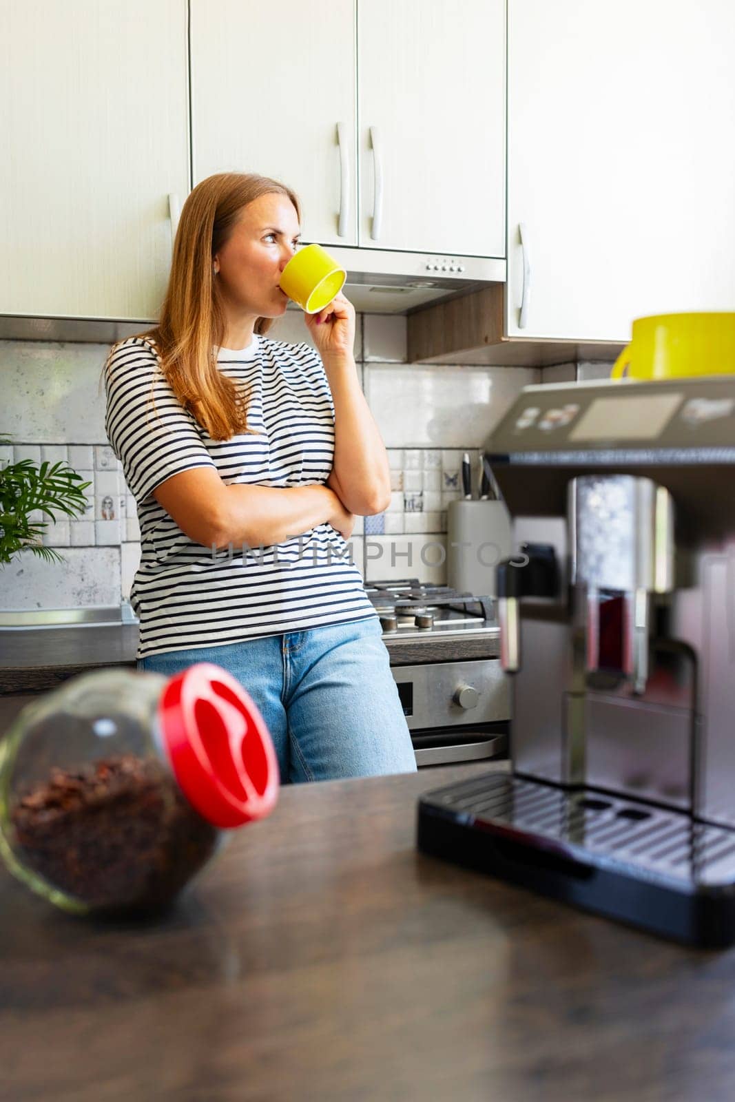 Young woman enjoying freshly prepared aromatic coffee near modern coffee machine in kitchen.