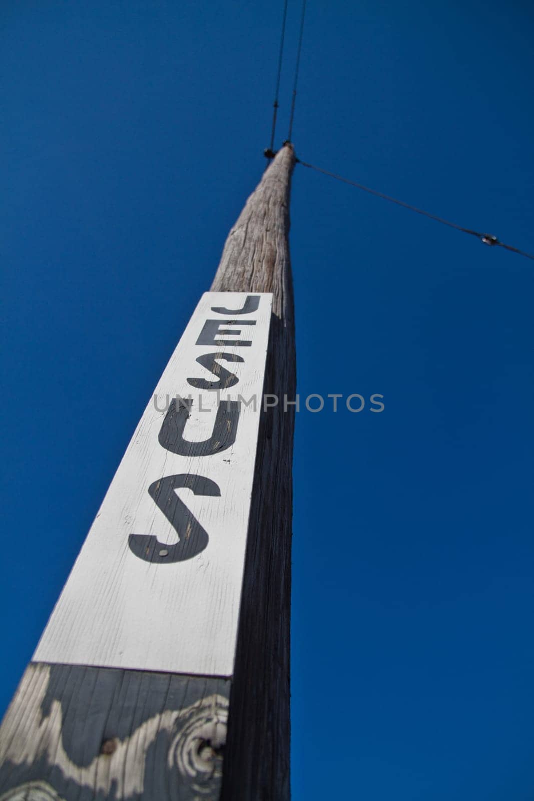 Rising Faith: A striking wooden utility pole against a clear blue sky features bold 'JESUS' lettering, evoking spirituality and reflection. Perfect for religious, inspirational, or communication-themed projects.